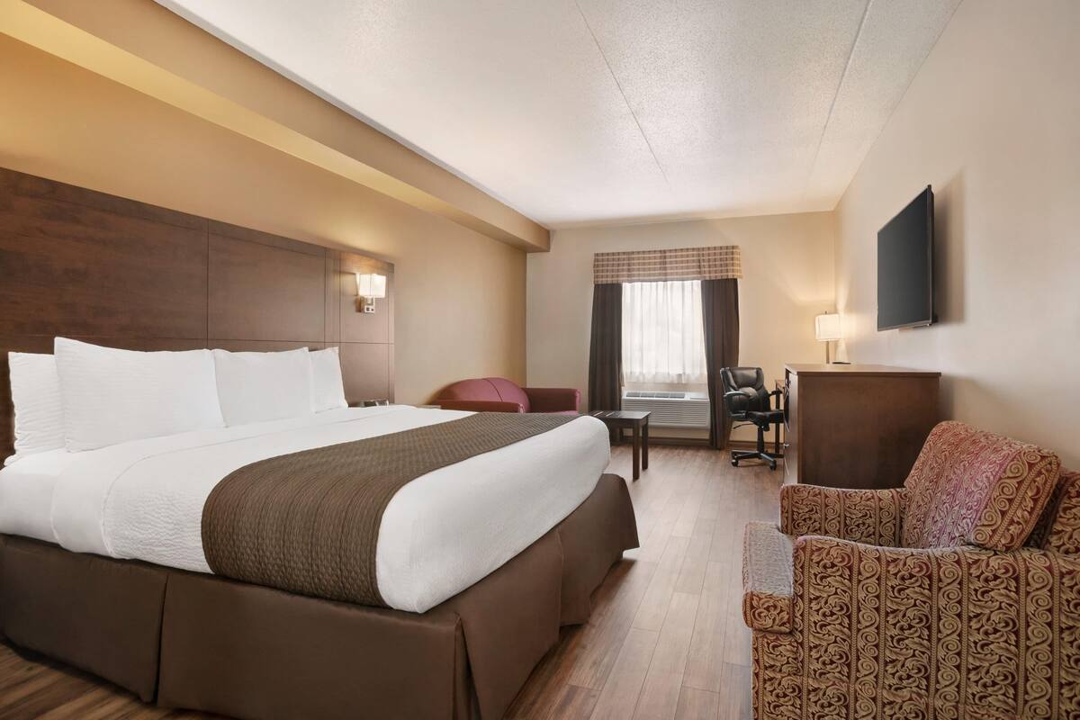 Une chambre d’hôtel avec un grand lit, un bureau, une chaise et un téléviseur fixé au mur.