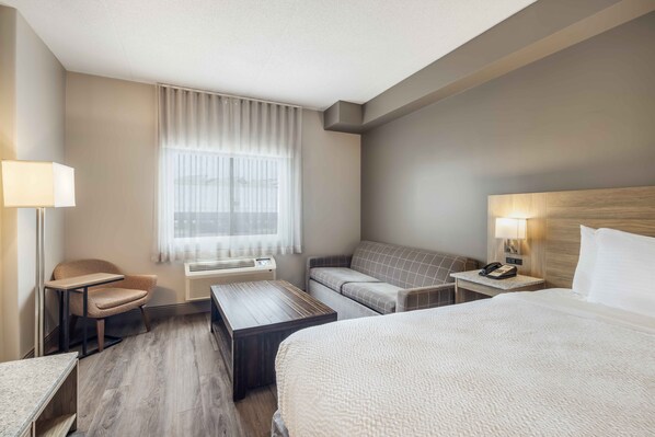 A hotel room with a bed, a sofa, a desk, a chair, a lamp, and a window with curtains.