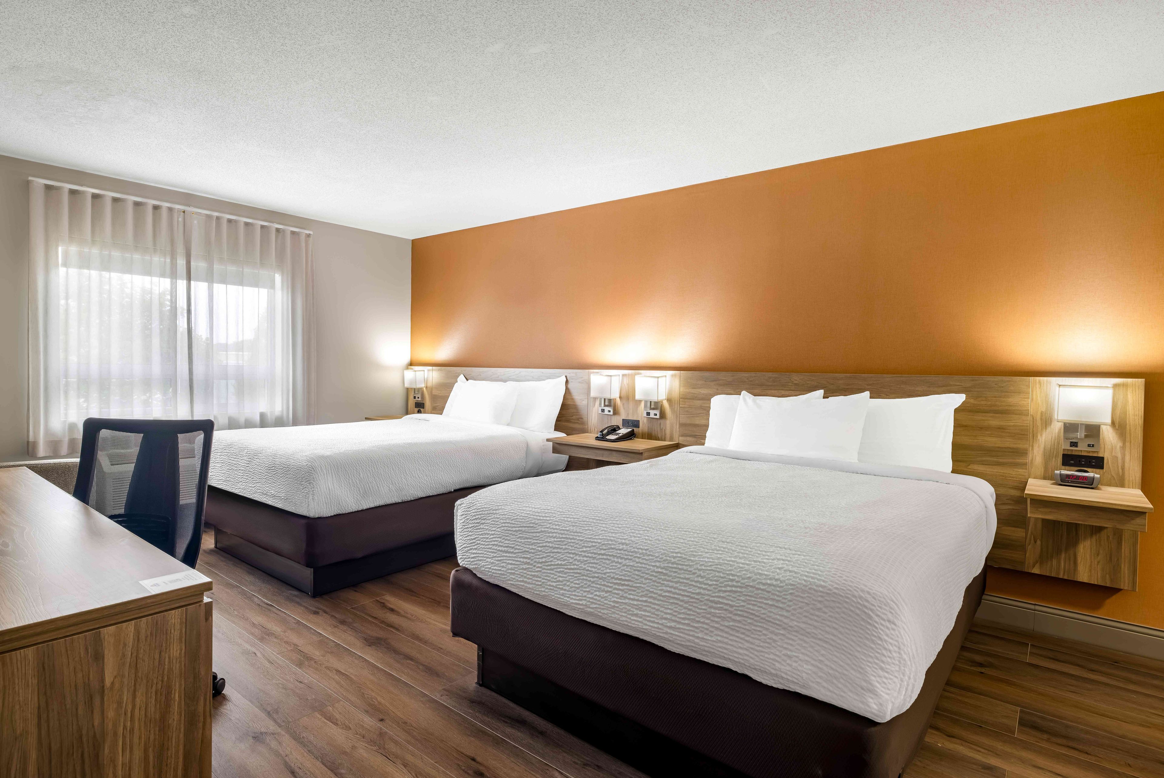 A hotel room with two beds, a desk, and a chair.
