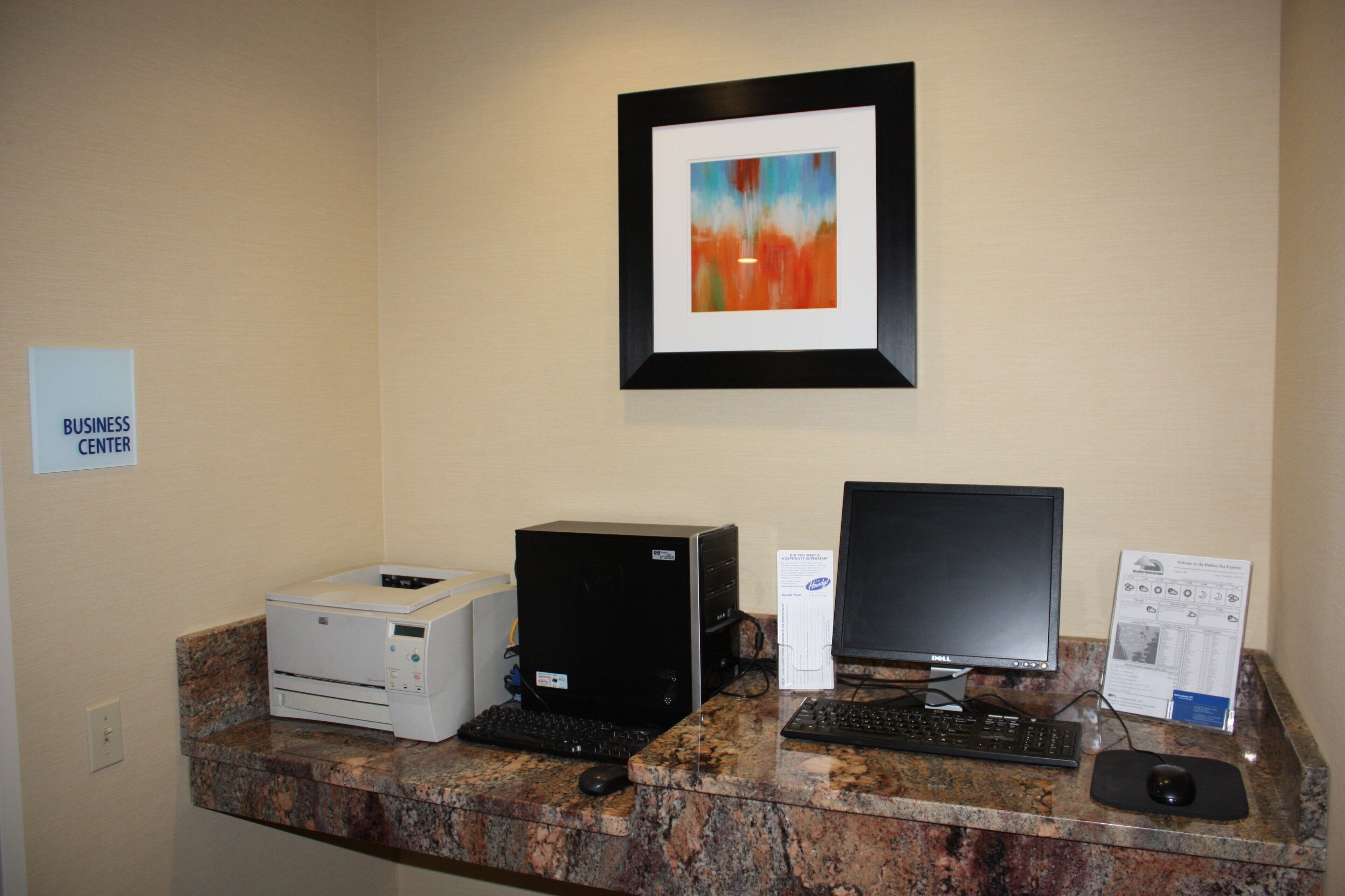 A reception desk with a computer, printer, and a framed abstract painting above it.