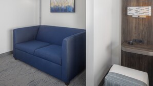 A modern room with a blue sofa, a floor lamp, a wall-mounted artwork, and a wooden panel with a light fixture. - Holiday Inn Express Ludlow by IHG (Ludlow)