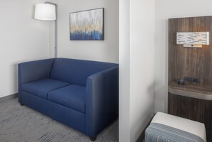 A modern room with a blue sofa, a floor lamp, a wall-mounted artwork, and a wooden panel with a light fixture. - Holiday Inn Express Ludlow by IHG (Ludlow)