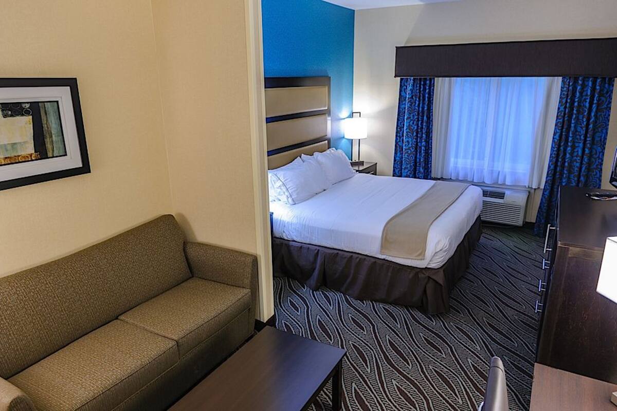 A hotel room with a bed, a sofa, a desk, and a framed picture on the wall.