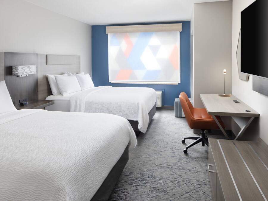 Ett hotellrum med två sängar, ett skrivbord, en stol, en TV och ett fönster med persienner.