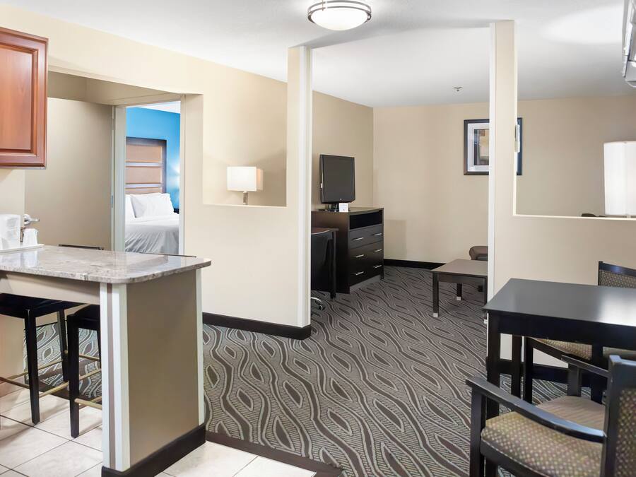 A hotel room with a kitchenette, a bed, a TV, a desk, and a dining area.