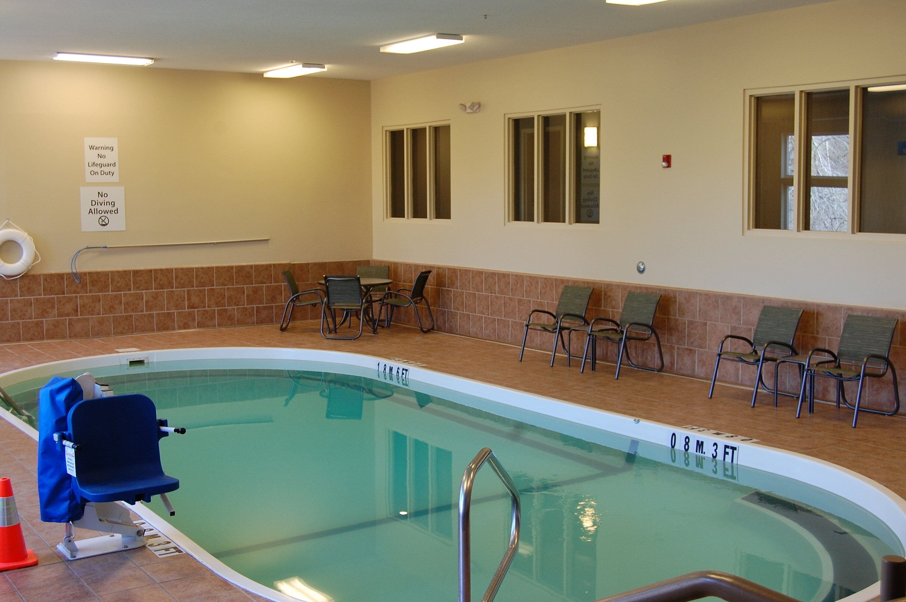 Une piscine intérieure équipée d’un poste de surveillance pour le sauveteur, de chaises au bord du bassin et d’un panneau indiquant qu’il est interdit de plonger.