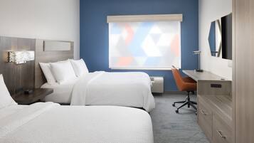 A hotel room with two beds, a desk, a chair, a TV, and a window with blinds.