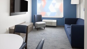 A hotel room with a flat-screen TV mounted on the wall, a dining table with chairs, a sofa, and a small ottoman. - Holiday Inn Express Ludlow by IHG (Ludlow)