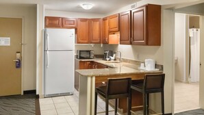 A compact kitchen with wooden cabinets, a white refrigerator, a microwave, a coffee maker, and a sink. There are two bar stools at the island. - Holiday Inn Express Ludlow by IHG (Ludlow)