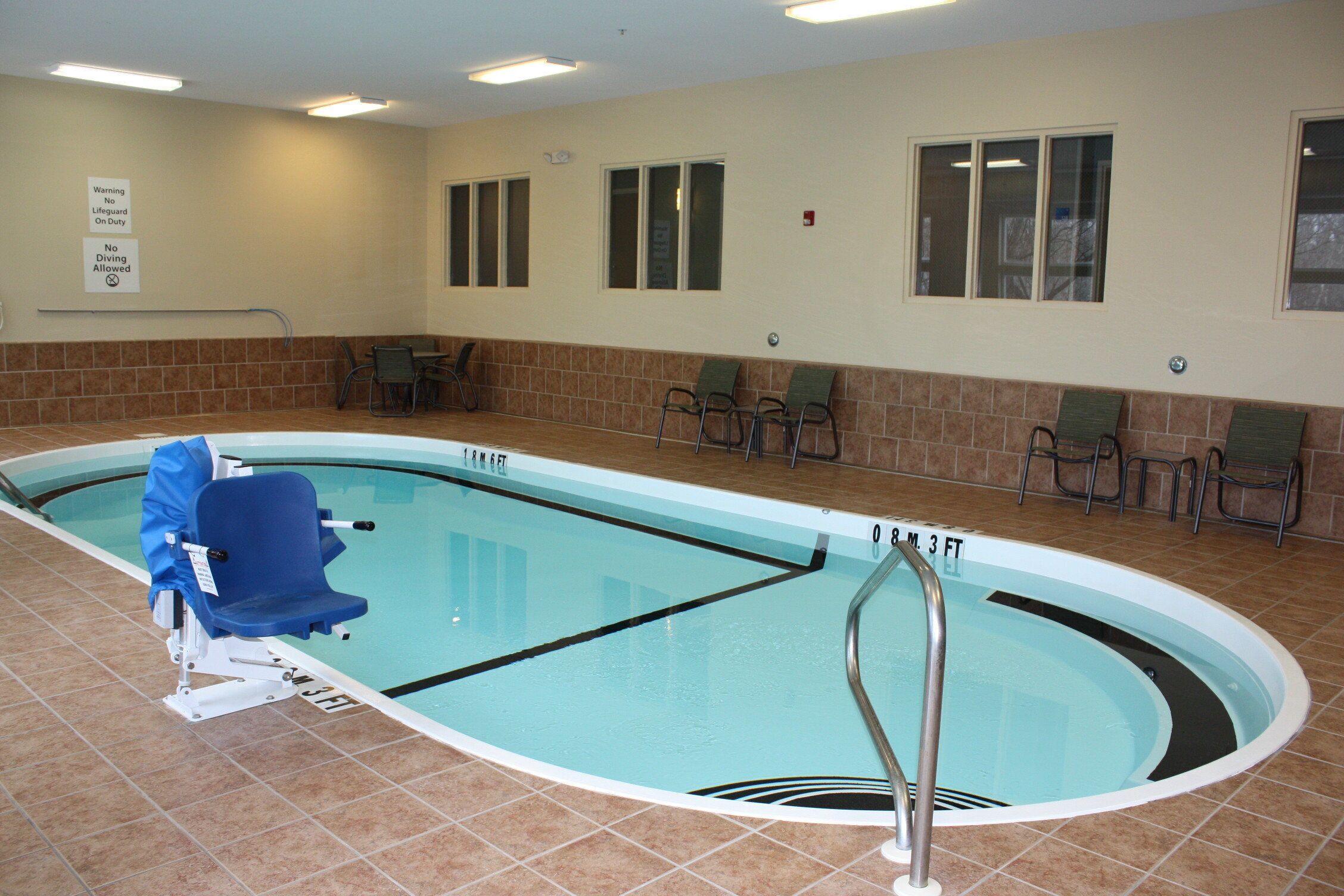 An indoor swimming pool with a lifeguard chair, pool depth markers, and a no diving allowed sign.
