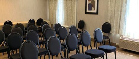 Una sala de conferencias con filas de sillas negras, una alfombra estampada, un techo con iluminación empotrada y un ventanal con cortinas.