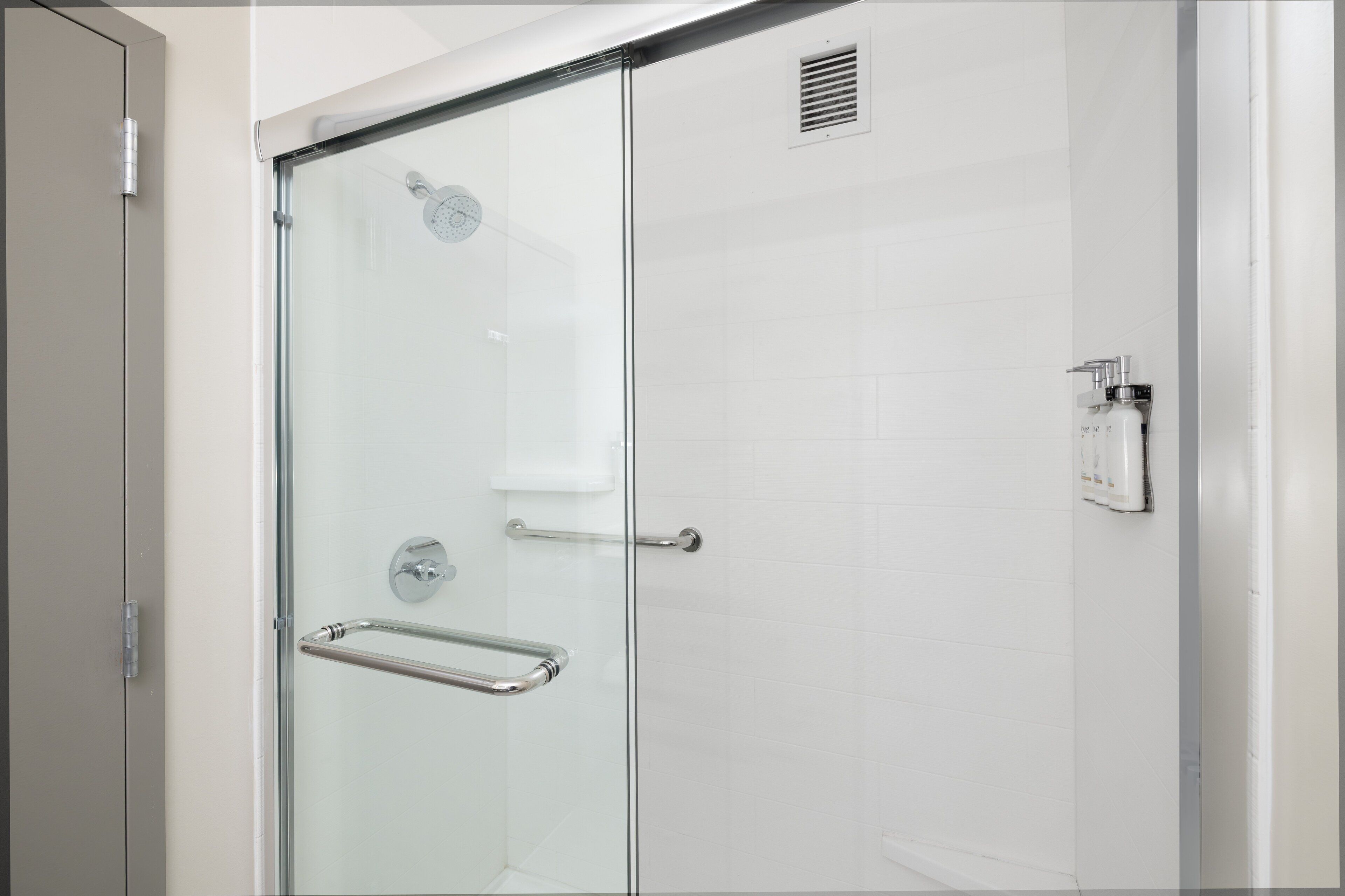 Una ducha moderna con puerta de vidrio, barra de apoyo y panel de control.