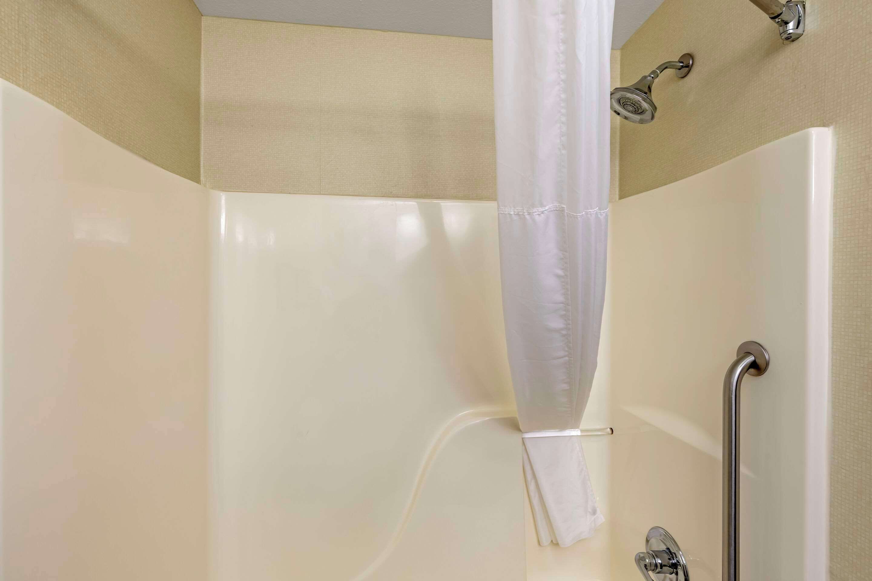 A shower with a white curtain, a handheld showerhead, and a grab bar.