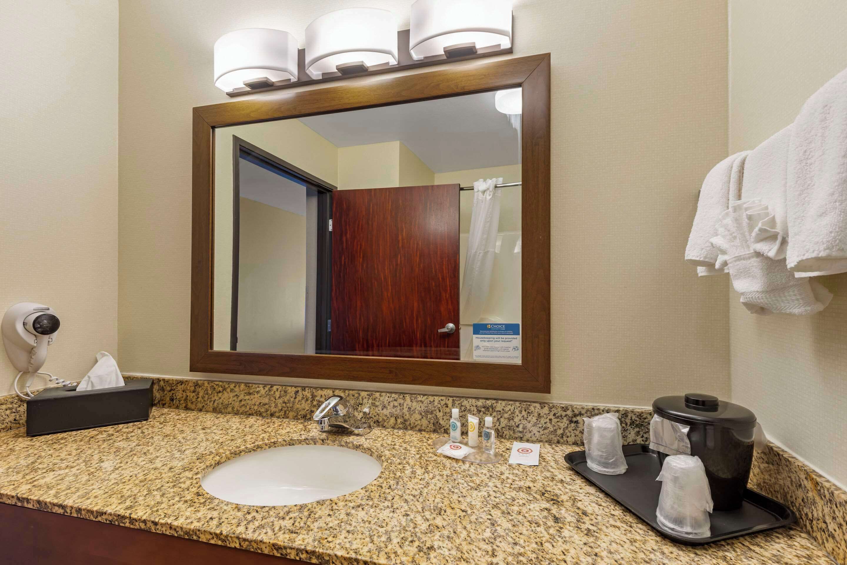 A hotel bathroom with a granite countertop, a sink, a mirror, a towel rack, and a security camera.