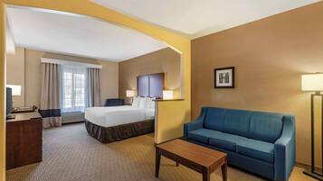 Quarto de hotel com uma cama, um sofá azul, uma mesa de centro de madeira, uma escrivaninha e um abajur.