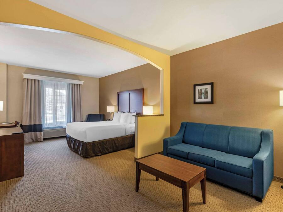 Quarto de hotel com uma cama, um sofá azul, uma mesa de centro de madeira, uma escrivaninha e um abajur.