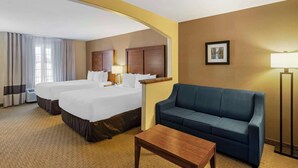 A hotel room with two beds, a sofa, a coffee table, and a lamp.