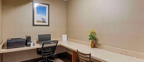 A hotel office with a desk, two chairs, a printer, a computer, and a framed picture on the wall.
