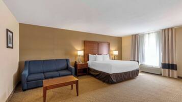A hotel room with a bed, a blue sofa, a wooden table, and a nightstand with lamps.