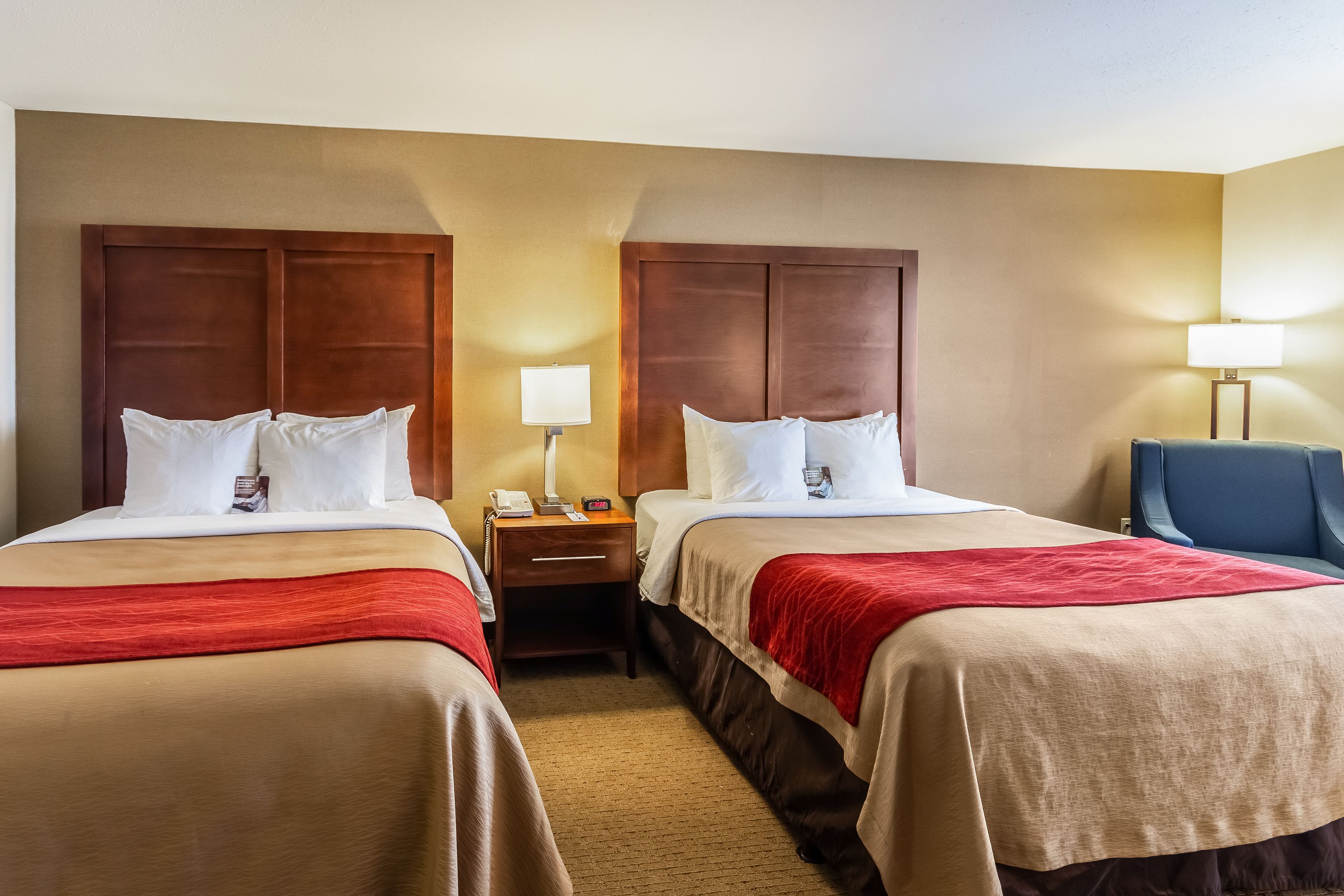 Une chambre d’hôtel avec deux lits, chacun doté d’une tête de lit en bois, d’une table de chevet avec une lampe et d’une chaise bleue.