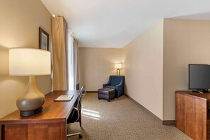 A hotel room with a wooden desk, a lamp, a chair, a television, and a small ottoman.