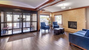 A lobby with a fireplace, blue armchairs, and a large glass door leading outside.