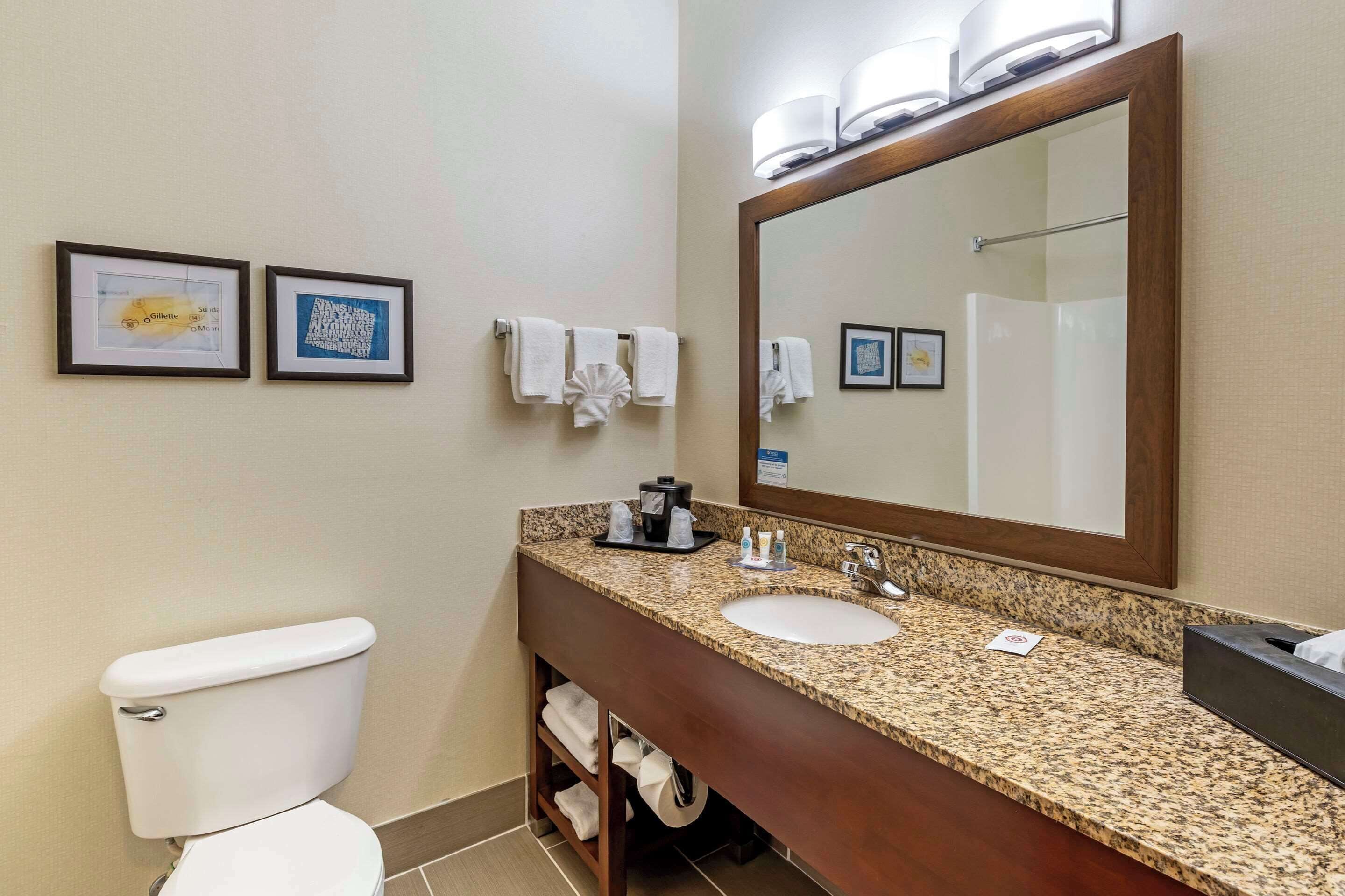 A bathroom with a toilet, sink, and large mirror. There are framed pictures on the wall and towels hanging on a rack.