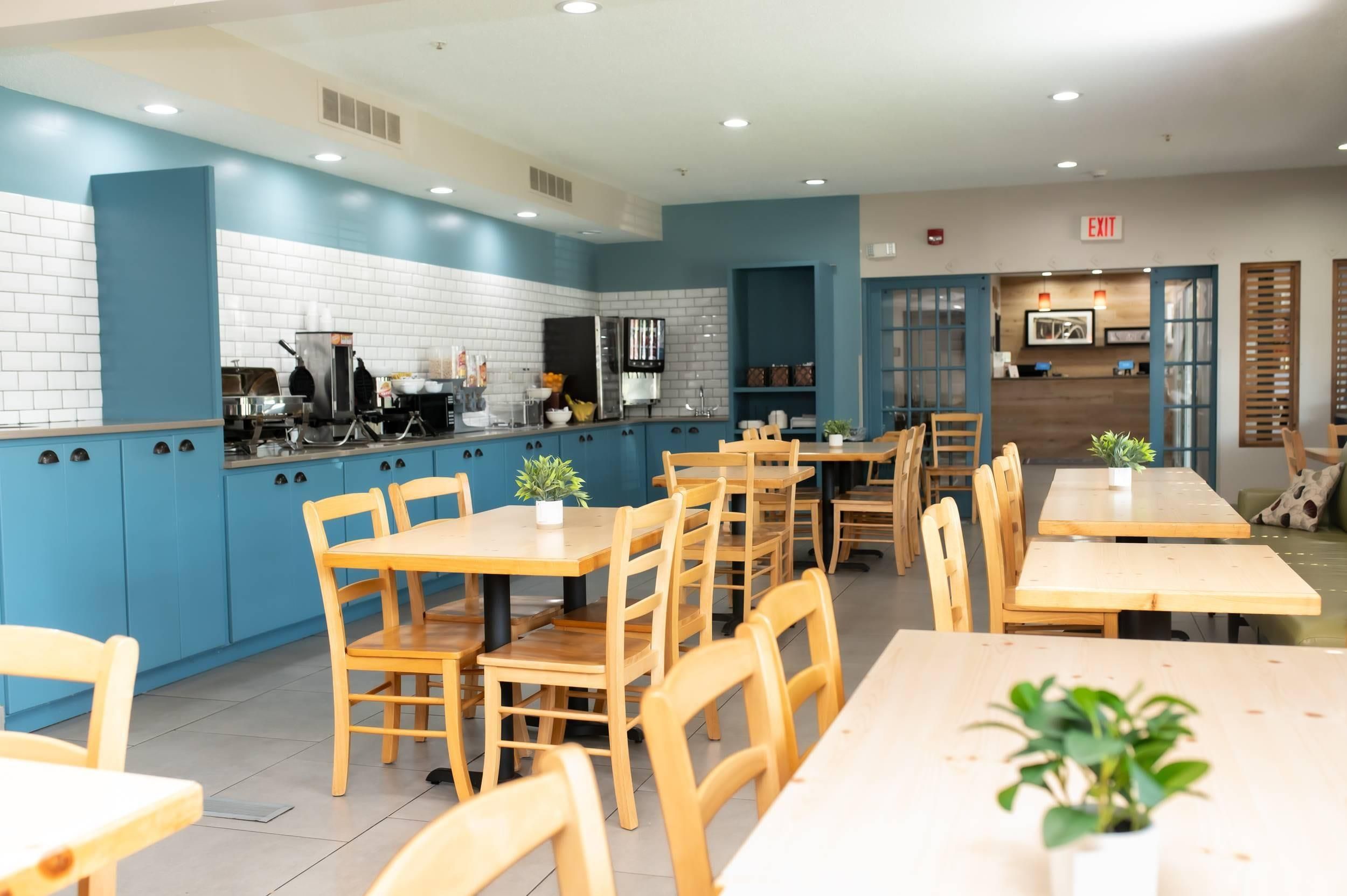 Un restaurante moderno con paredes de azulejos azules y blancos, mesas y sillas de madera, y una zona de cocina visible al fondo.