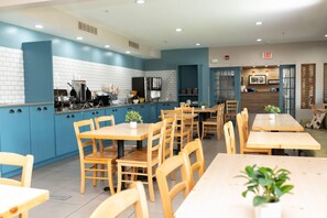 Un restaurante moderno con paredes de azulejos azules y blancos, mesas y sillas de madera, y una zona de cocina visible al fondo.