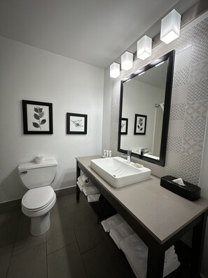 A modern bathroom with a toilet, sink, and large mirror. There are framed pictures on the wall and a towel rack. - Country Inn & Suites by Radisson, Prairie du Chien (Prairie Du Chien)