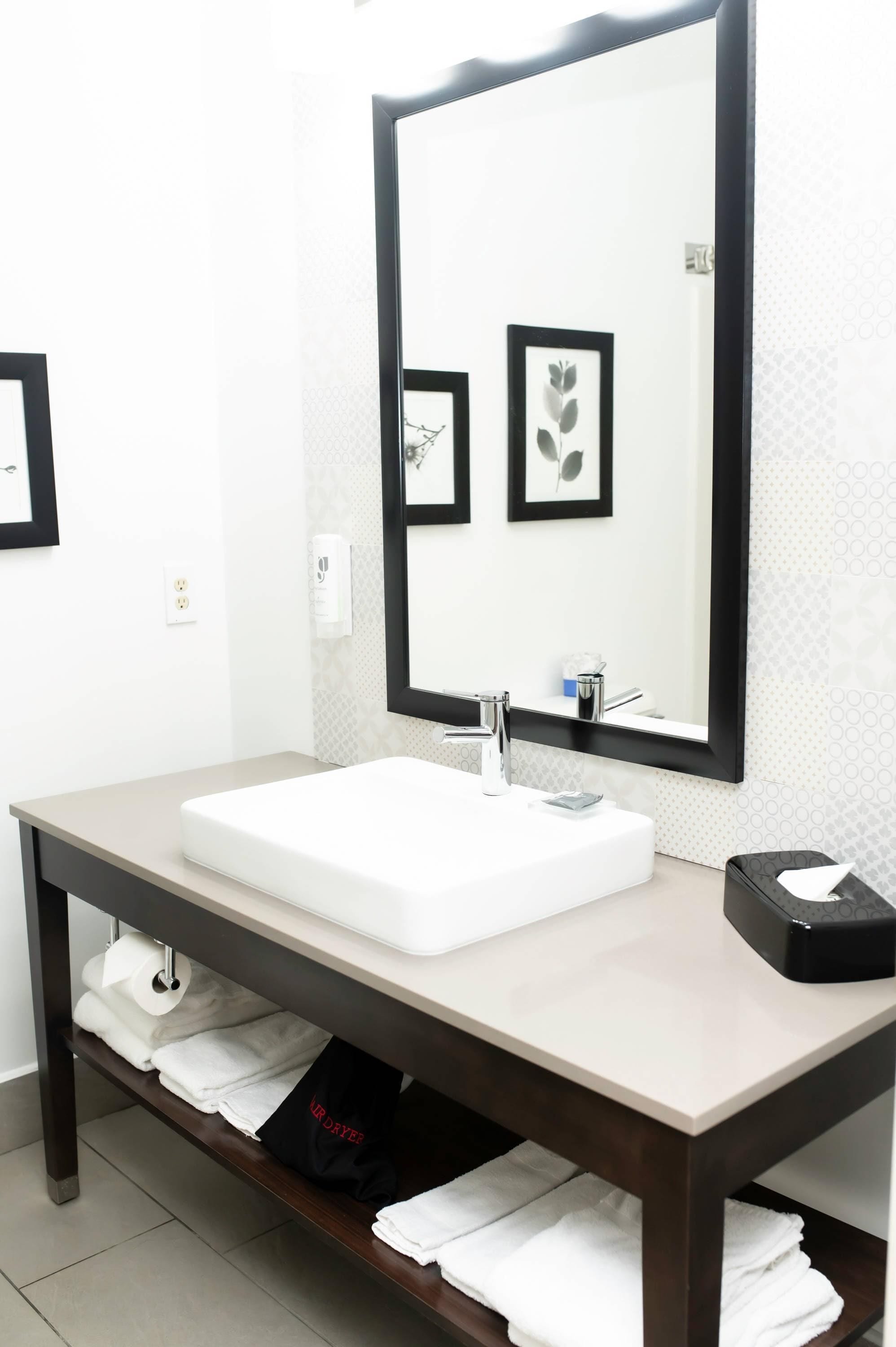 A modern bathroom with a large mirror, white sink, and a towel rack under the sink.