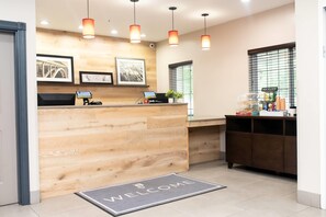 A reception area with a wooden reception desk, a laptop, framed pictures on the wall, and a welcome mat. - Country Inn & Suites by Radisson, Prairie du Chien (Prairie Du Chien)