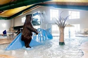 Un oso en un parque acuático interior con toboganes y una estructura con forma de árbol.