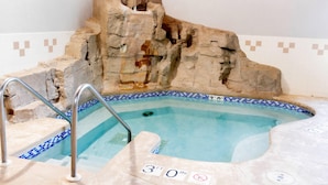 Un bain à remous avec un décor rocheux, un bord carrelé et un escalier en métal.