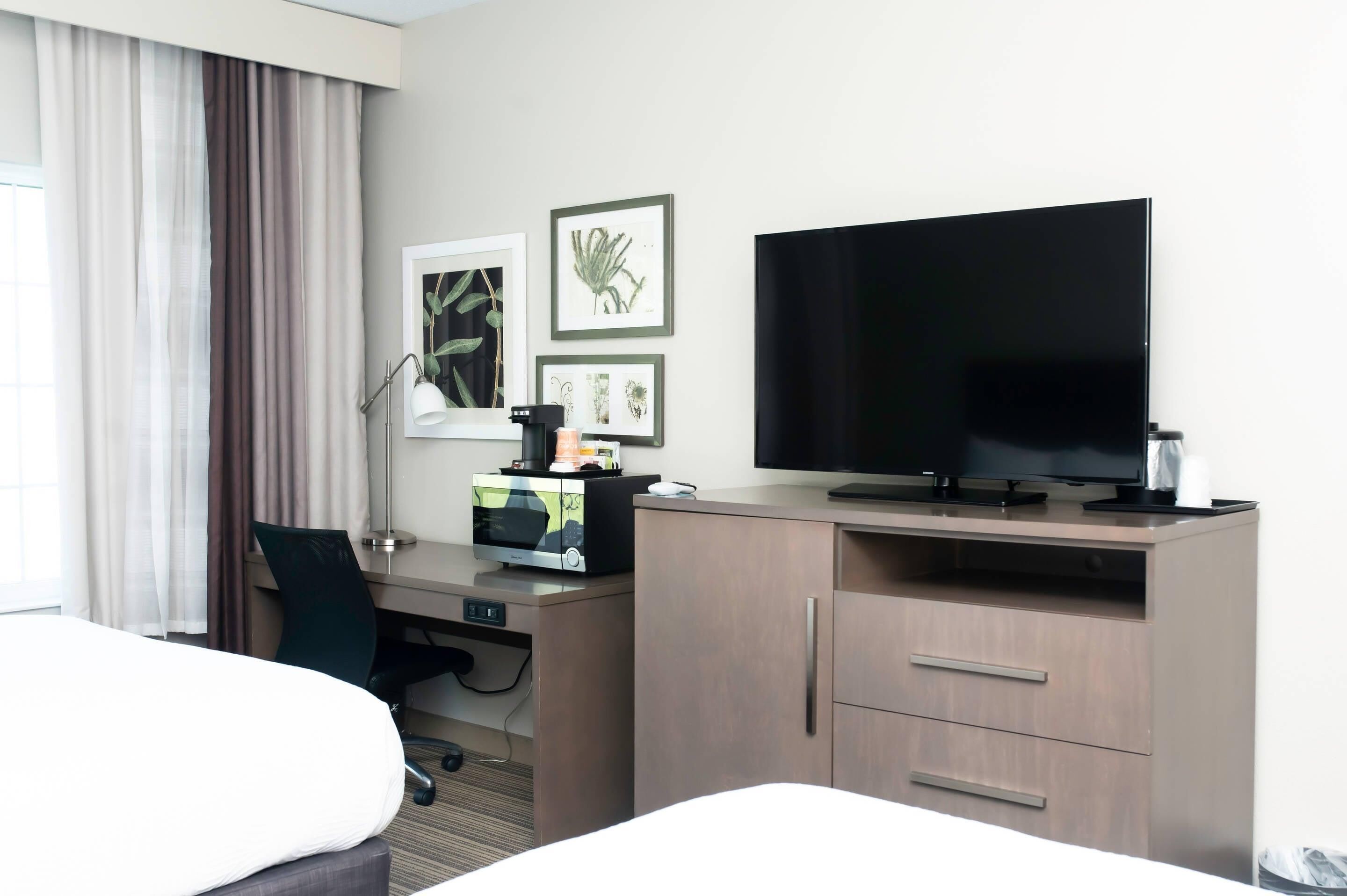 A hotel room with a bed, desk, TV, and artwork on the wall.