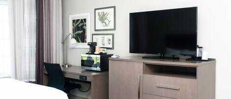 A hotel room with a bed, desk, TV, and artwork on the wall.