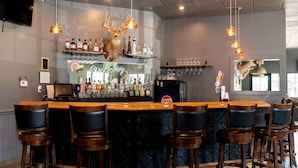 Un espace bar avec un comptoir en bois, des tabourets de bar noirs et une tête de cerf accrochée au mur.