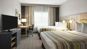 Une chambre d’hôtel avec un lit, un bureau avec un ordinateur, une télévision et une fenêtre avec des rideaux.