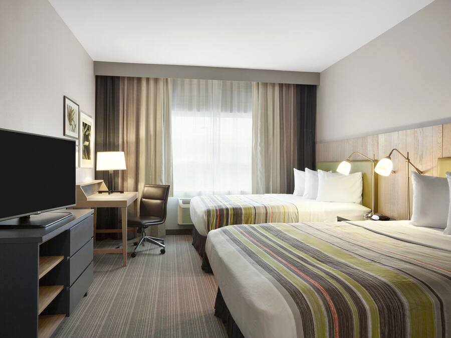 Habitació d'hotel amb llit, escriptori amb ordinador, televisió i finestra amb cortines.