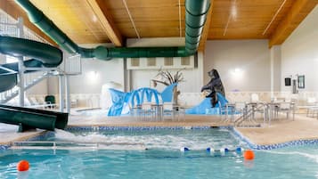 An indoor swimming pool with a water slide, seating area, and a statue.