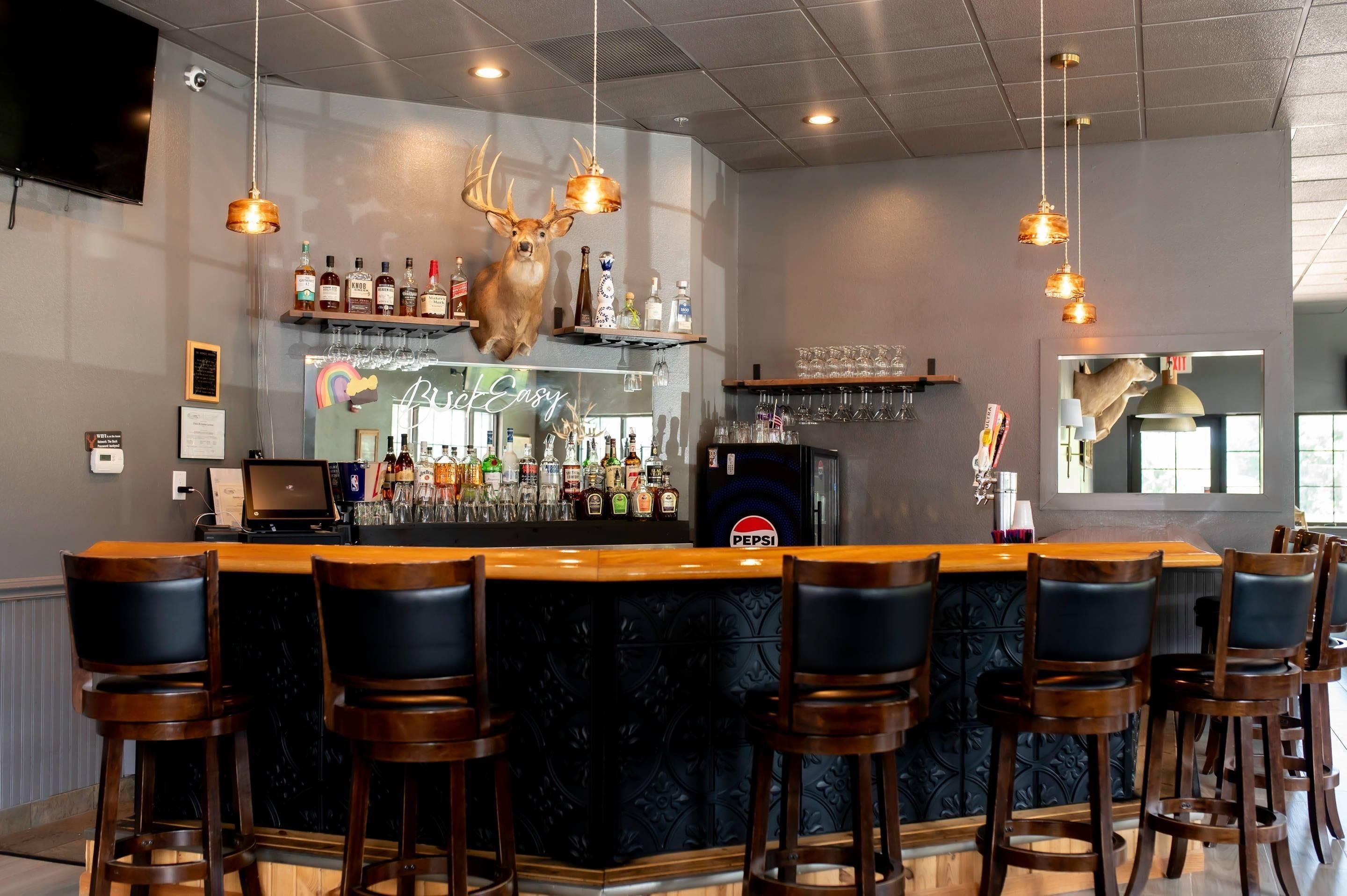 A bar area with a wooden counter, black bar stools, and a mounted deer head.