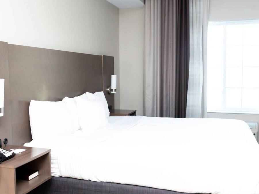A hotel room with a bed, a bedside telephone, a nightstand, a wall-mounted lamp, and a window with curtains.