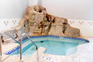 A hot tub with a rocky backdrop, a metal ladder, and a tiled edge.