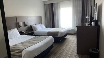 Habitación de hotel con dos camas, un escritorio, una silla, una lámpara y una ventana con cortinas.