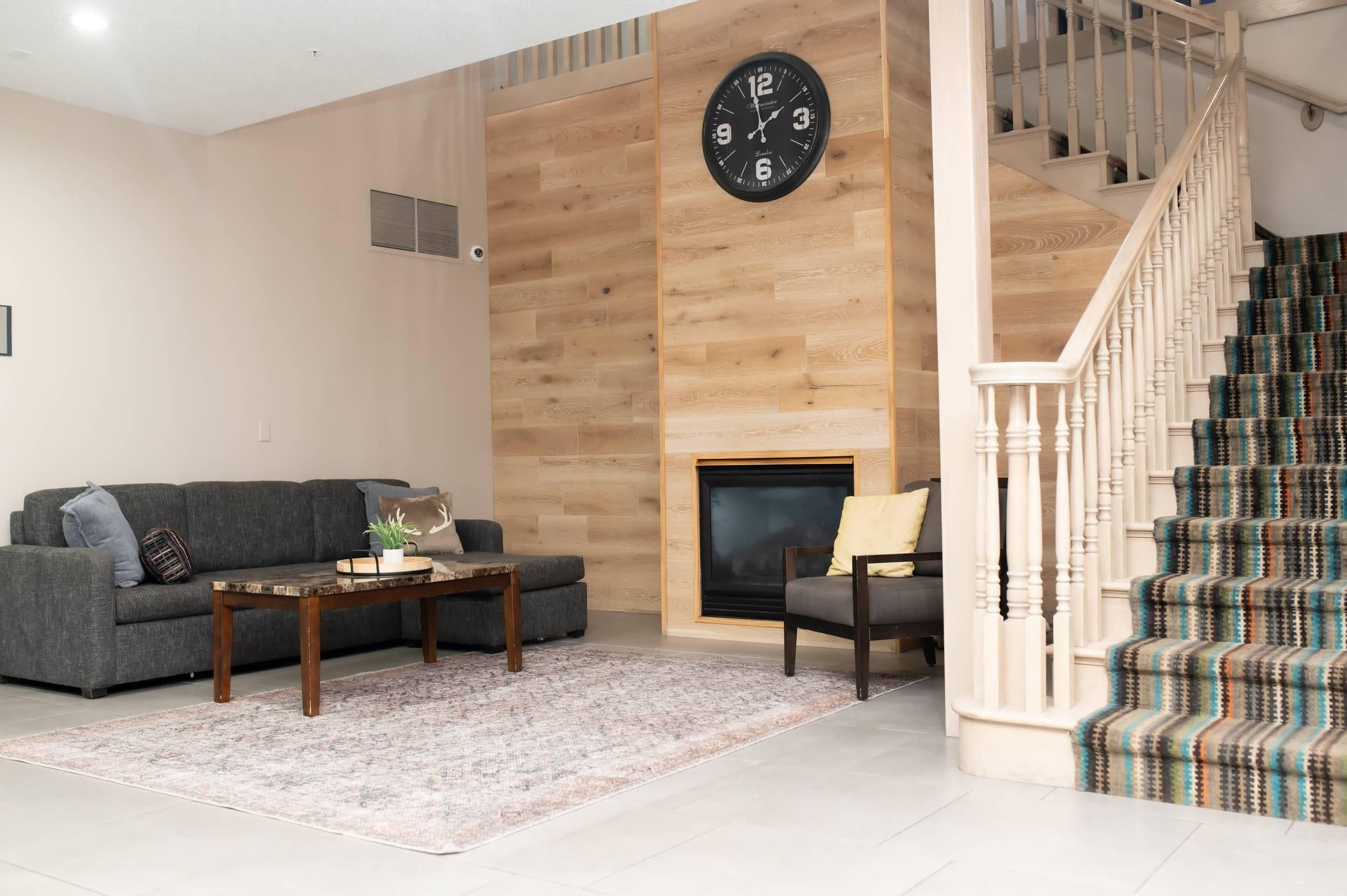 A living room with a sofa, coffee table, and fireplace. A staircase with patterned carpet leads to an upper floor.