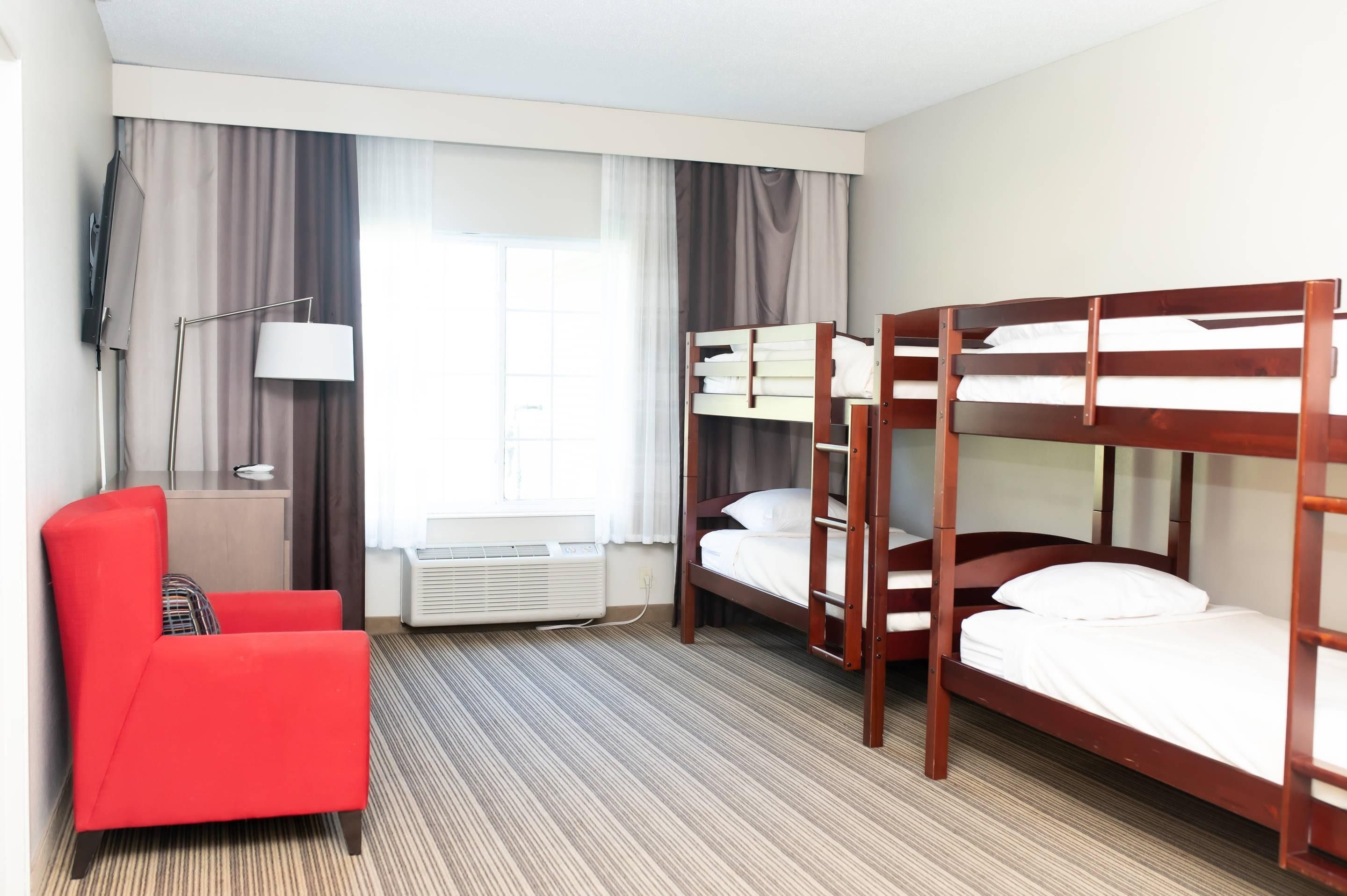 A hotel room with a red armchair, a TV, a desk with a lamp, and two bunk beds.