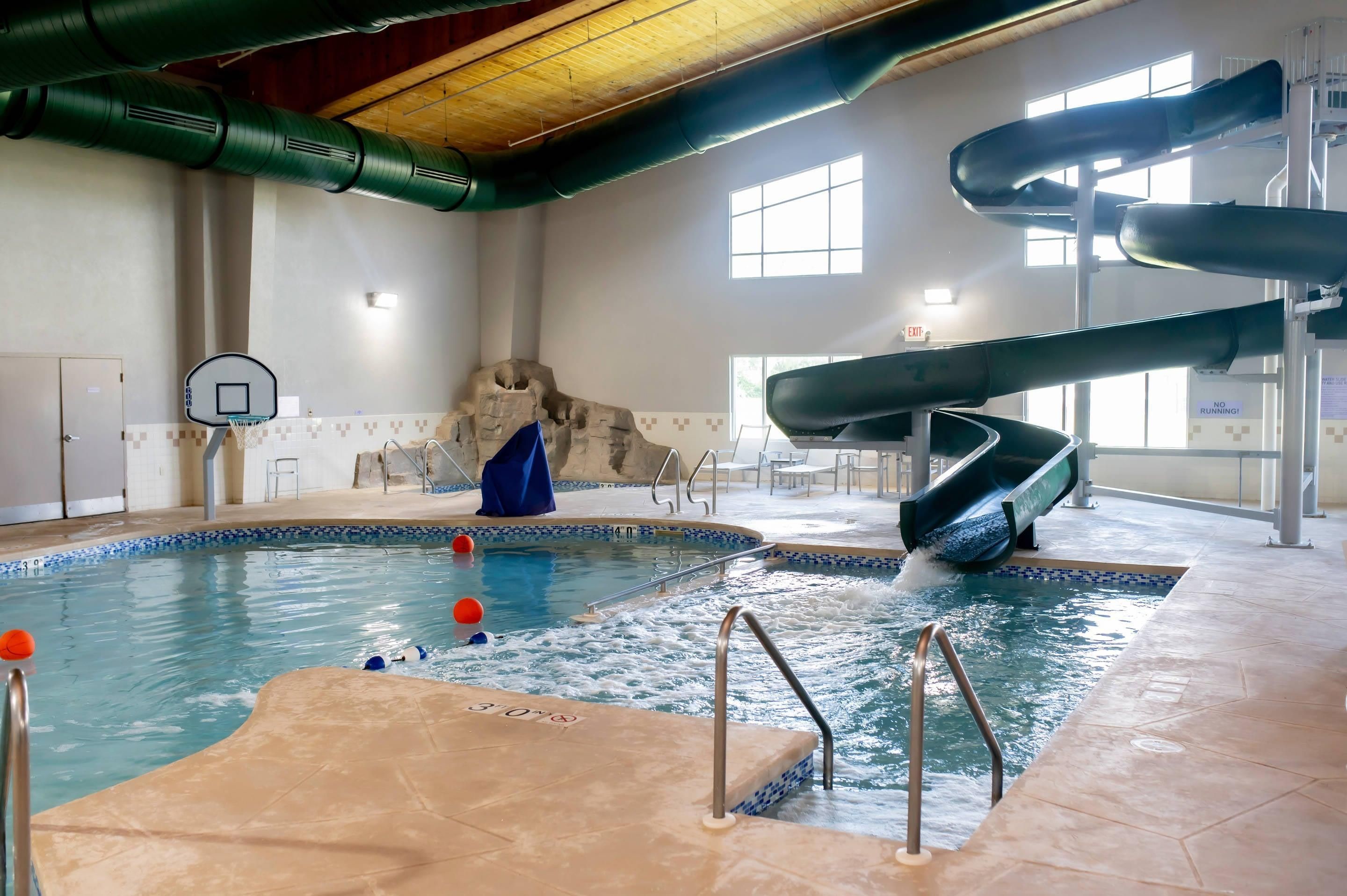 An indoor pool with a basketball hoop, a slide, and a rock wall.