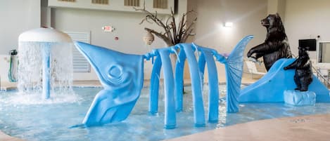 Una fuente con una estatua de oso y una escultura de pez azul en un área de piscina.