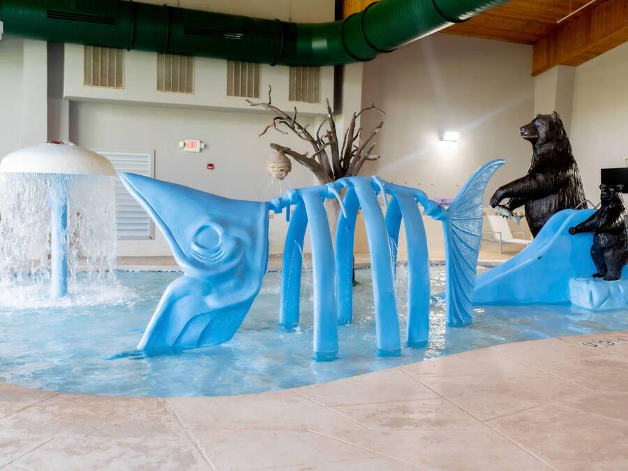 A water feature with a bear statue and a blue fish sculpture in a pool area.