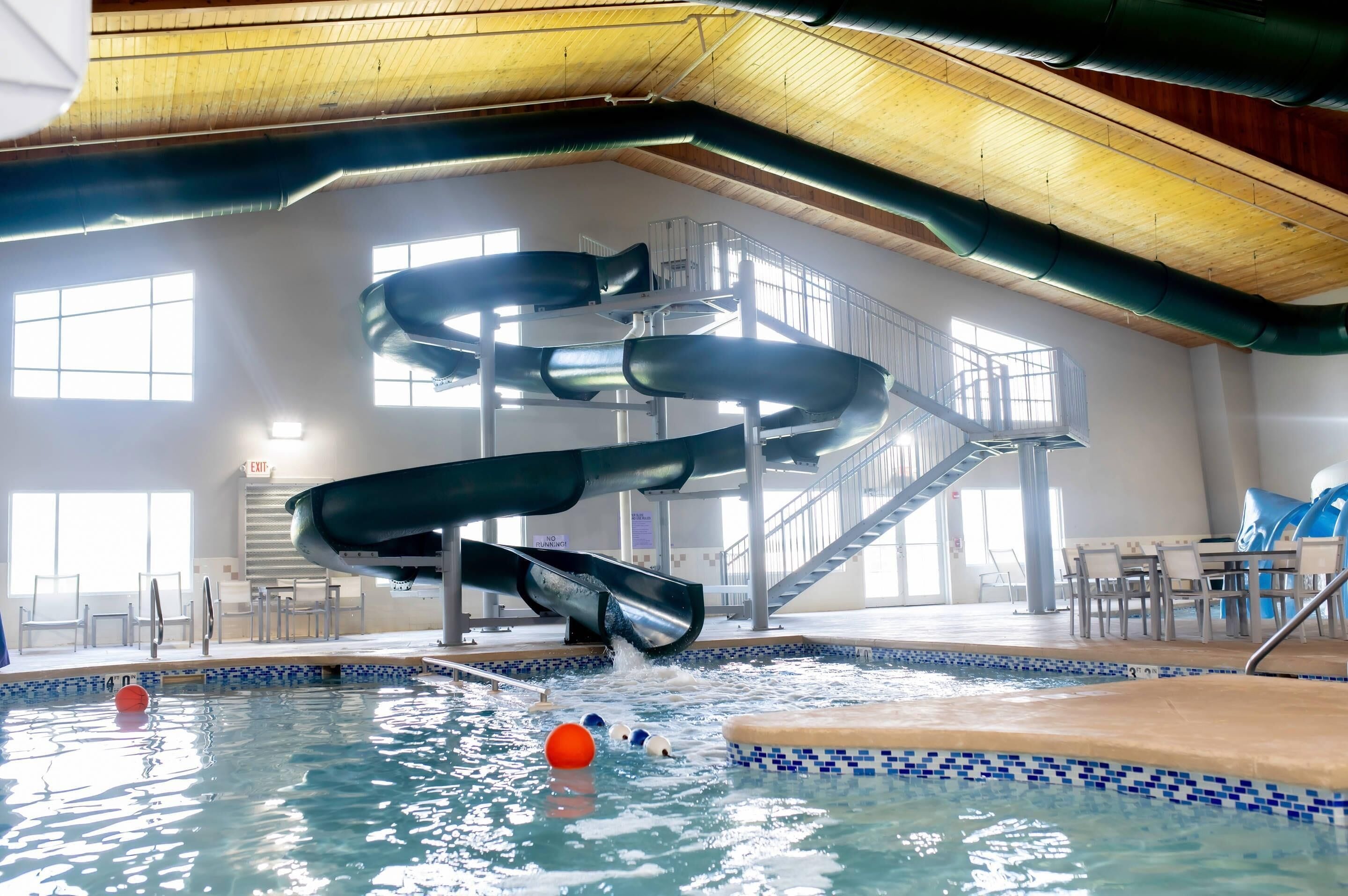 An indoor swimming pool with multiple slides, a tiled floor, and a staircase leading to a mezzanine.